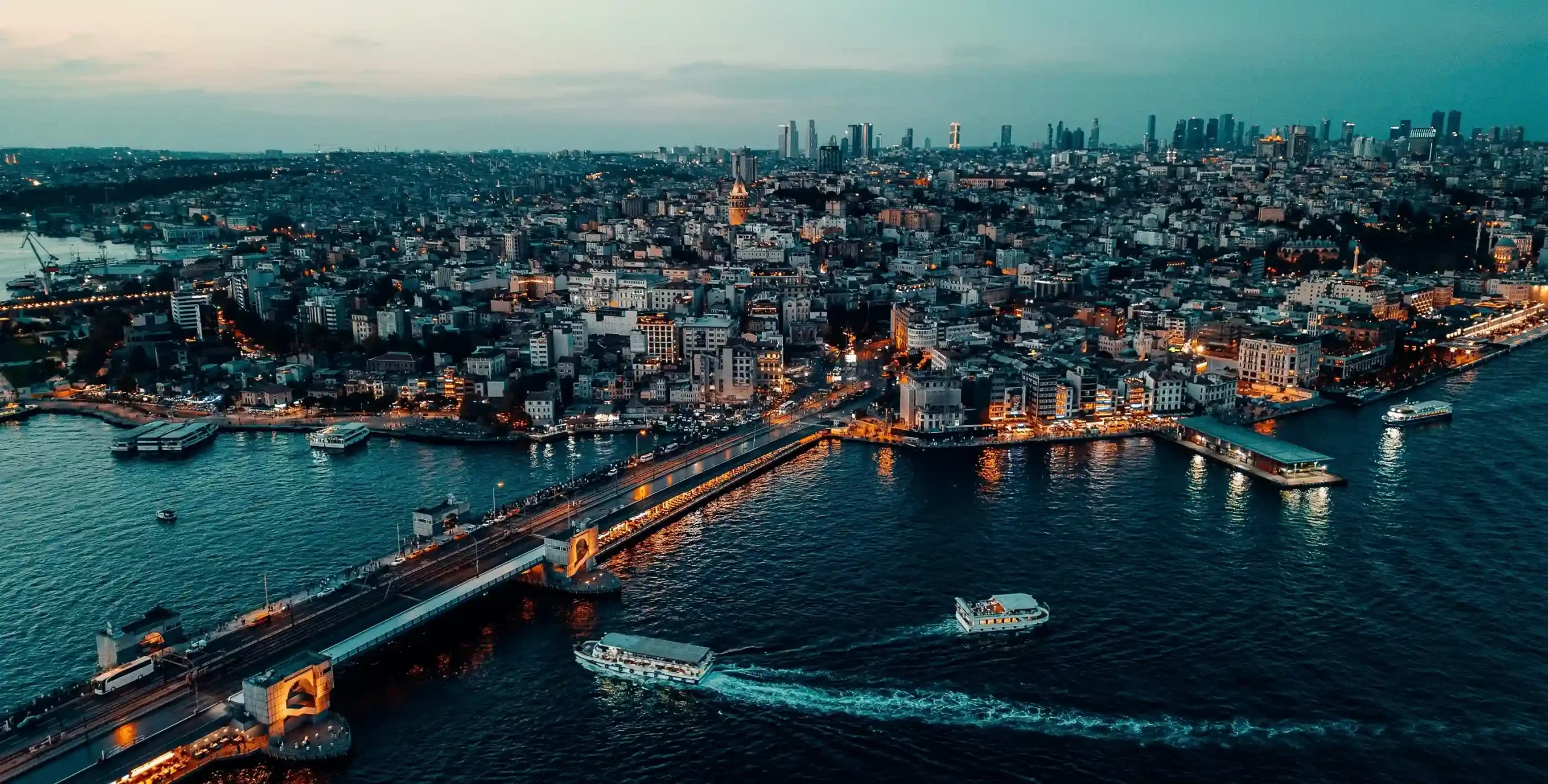 Aerial view of Galata Bridge and the Golden Horn in Istanbul at dusk, with Beyoğlu and the Istanbul skyline in the background